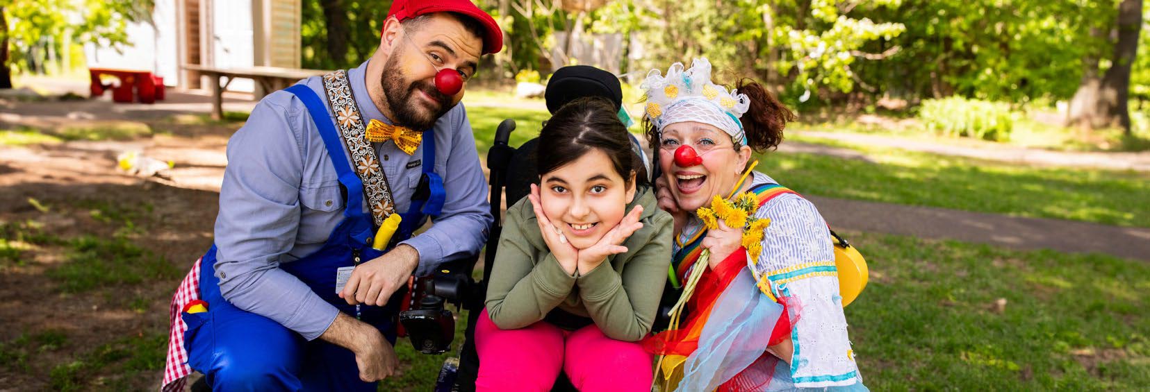 Two clowns with a child on wheelchair